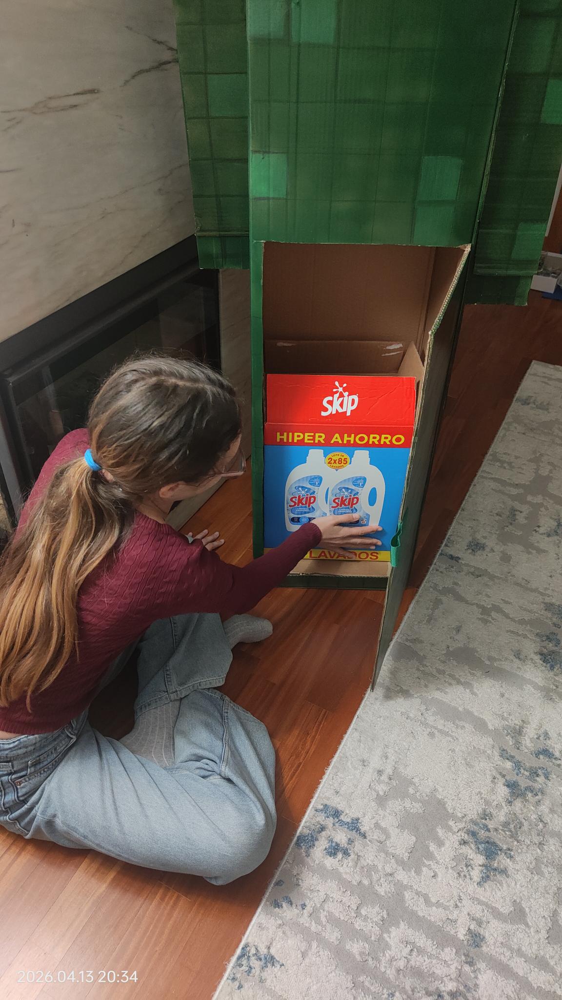 A aluna a experimentar a caixa de detergente de lavar roupa para comprovar que as medidas correspondem às desejadas para o seu Traga-pilhas. Posteriormente pintou a caixa de cartão de Skip.